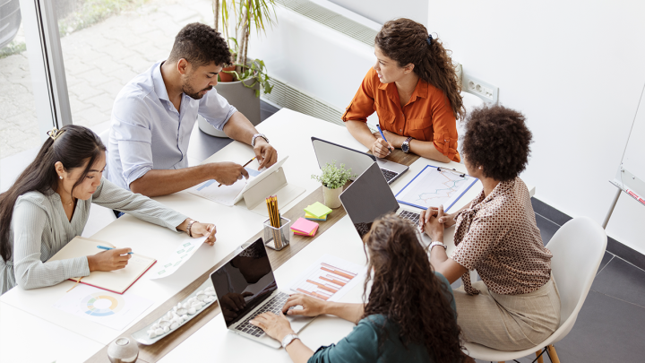 five colleagues sitting at a shared desk discussing work 