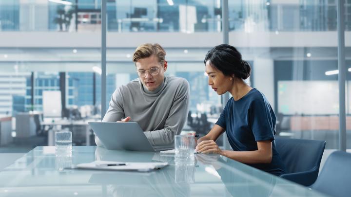 Two professionals in a modern office reviewing data on a laptop