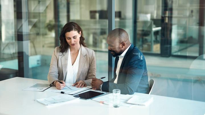 Two professionals reviewing business documents and technology planning materials during a meeting.