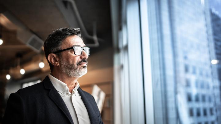 Business professional looking out of an office window overlooking a city while considering strategic technology decisions.