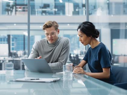 Two professionals in a modern office reviewing data on a laptop