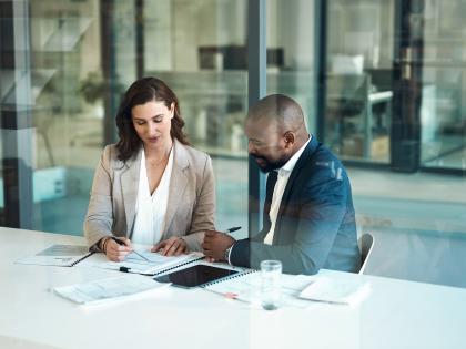 Two professionals reviewing business documents and technology planning materials during a meeting.