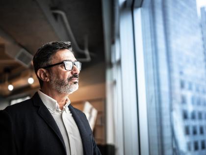 Business professional looking out of an office window overlooking a city while considering strategic technology decisions.