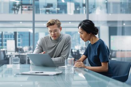 Two professionals in a modern office reviewing data on a laptop