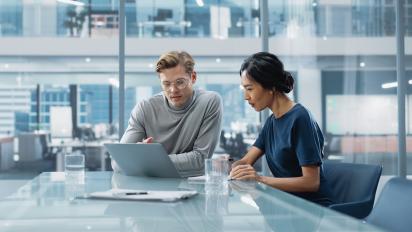 Two professionals in a modern office reviewing data on a laptop